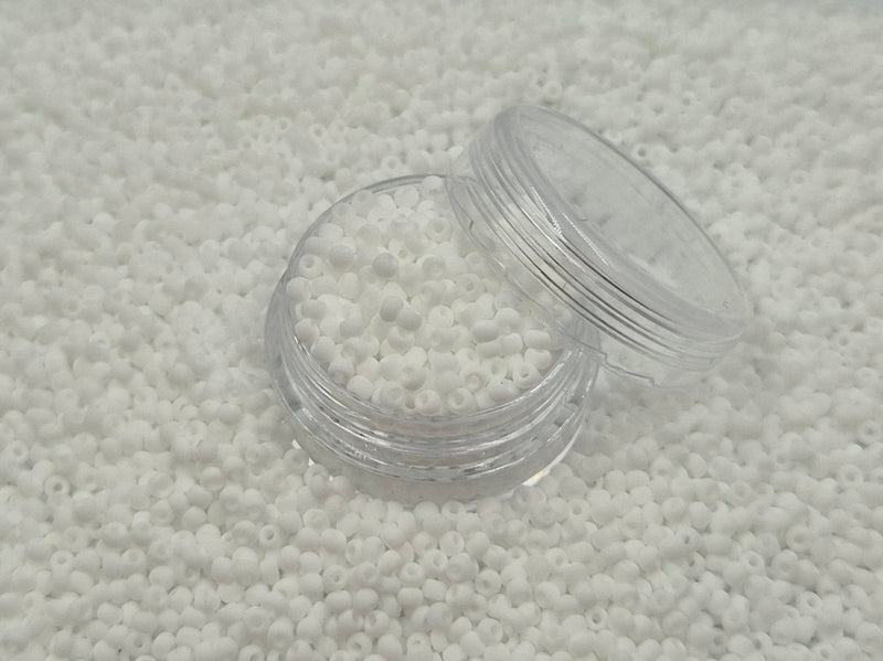 Små, runde, matte hvide perler i en gennemsigtig plastikbeholder, som står på en masse perler af samme art. 