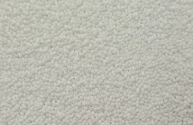 Små, runde, matte hvide perler i en gennemsigtig plastikbeholder, hvor de falder lidt ud af, og ligger på en grå baggrund. 