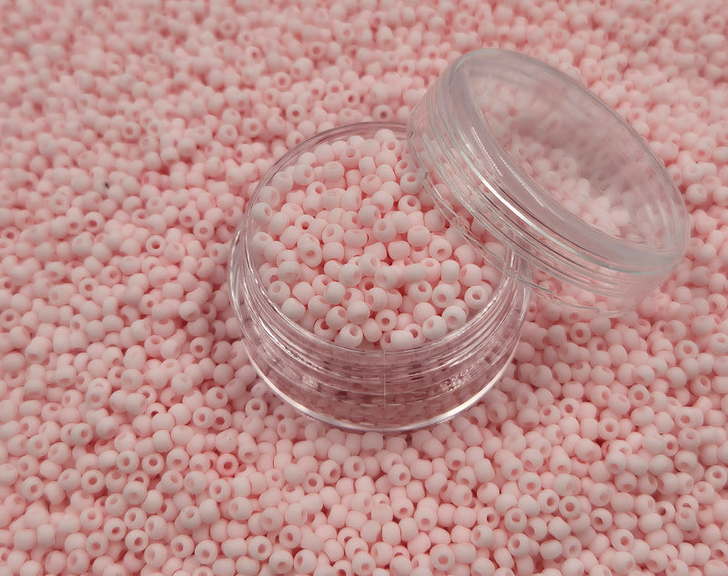 Små, runde, matte lyserøde perler i en gennemsigtig plastikbeholder, som står på en masse perler af samme art. 