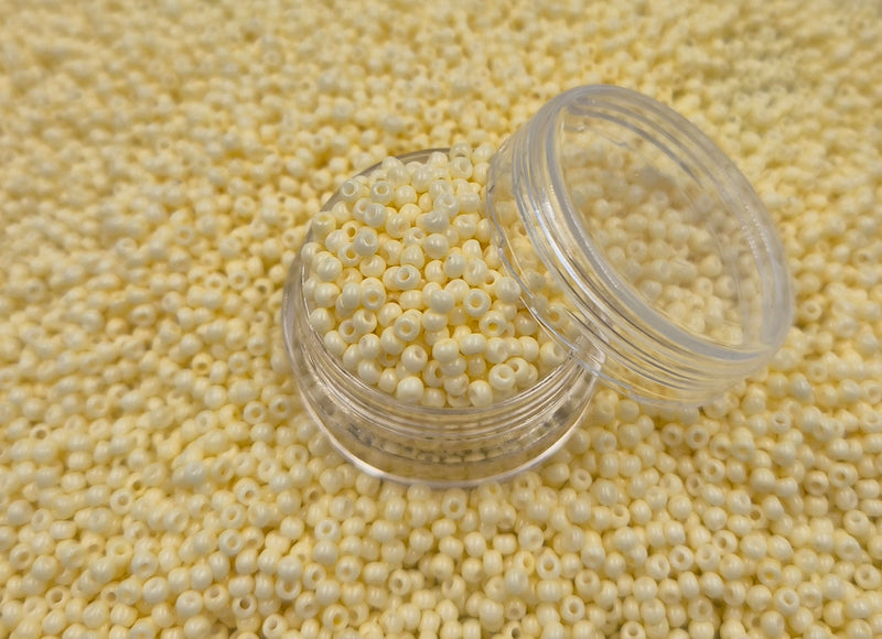 Små, runde, elfenbens-farvede perler i en gennemsigtig plastikbeholder, som står på en masse perler af samme art. 
