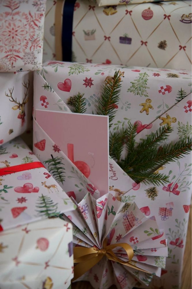 Gavepapiret "Mistletoe" på indpakkede gaver, med snor om, lidt gran, og nogle kort. På gavepapiret er der både mistelten, svampe, sløjfer, juletræer, rådyr, gaver og gingerbread kagemænd. 