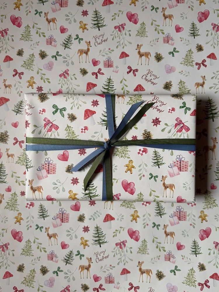 Gavepapiret "Mistletoe" som underlag og på en indpakket gave, med snor om. På gavepapiret er der både mistelten, svampe, sløjfer, juletræer, rådyr, gaver og gingerbread kagemænd. 