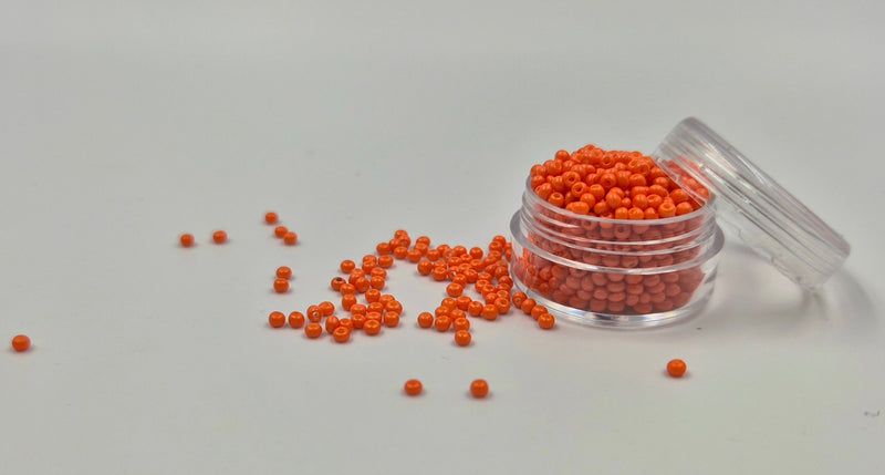 Små, runde, orange perler i en gennemsigtig plastikbeholder, hvor de falder lidt ud af, og ligger på en grå baggrund. 