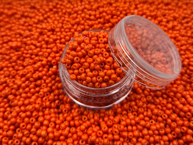 Små, runde, orange perler i en gennemsigtig plastikbeholder, som står på en masse perler af samme art. 