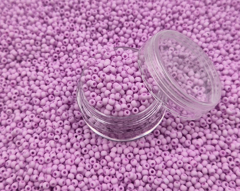 Små, runde, matte pastel-rosa perler i en gennemsigtig plastikbeholder, hvor de falder lidt ud af, og ligger på en grå baggrund. 