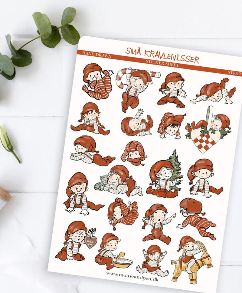 Et billede af Julenisse klistermærker, der lægger på en hvid træbaggrund, med nogle grene med grønne blade på i siden. 