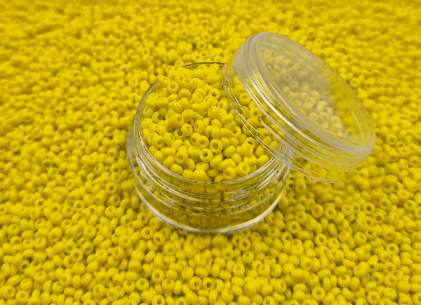 Små, runde, solsikke gule perler i en gennemsigtig plastikbeholder, som står på en masse perler af samme art. 