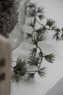 Et stemningsbillede med vaser med kogler i, og en grøn gren der ligger hen over en bord. 