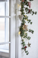 Et stemningsbillede af en gran guirlande, med en lyskæde og julepynt i, der hænger ned at siden af en glasdør indenfor. 