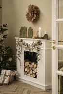 Et stemningsbillede, af en pejs med brænde i, et pyntet juletræ med gaver under ved siden af, kalenderlys og pynt på pejsen, og mere pynt rundt om. 