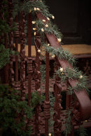 Et stemningsbillede, af en gran guirlande med en lyskæde omkring, som hænger på et rødt trappe gelænder. 